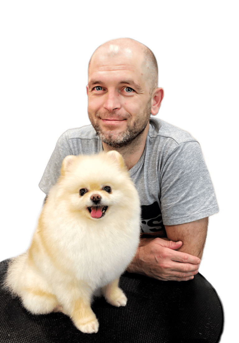 Лисий чоловік з бородою сперся на круглий столик, на якому сидить маленький кремовий шпіц