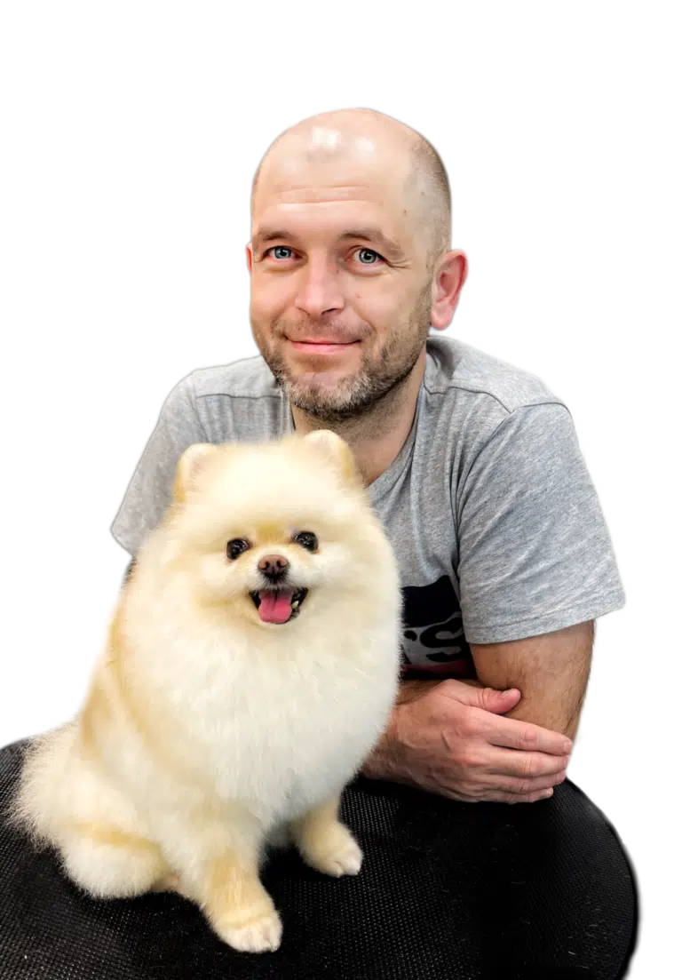 Лисий чоловік з бородою сперся на круглий столик, на якому сидить маленький кремовий шпіц