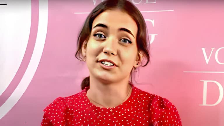 Рудоволоса дівчина в червоній блузі з білими горошинками розповідає щось на камеру