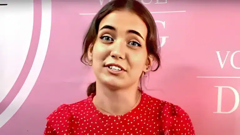 Рудоволоса дівчина в червоній блузі з білими горошинками розповідає щось на камеру