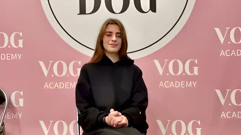 Дівчина міцно тримає разом свої руки, сидячи на фоні рожевої стіни з написами