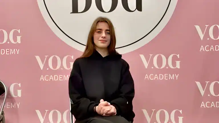 Дівчина міцно тримає разом свої руки, сидячи на фоні рожевої стіни з написами