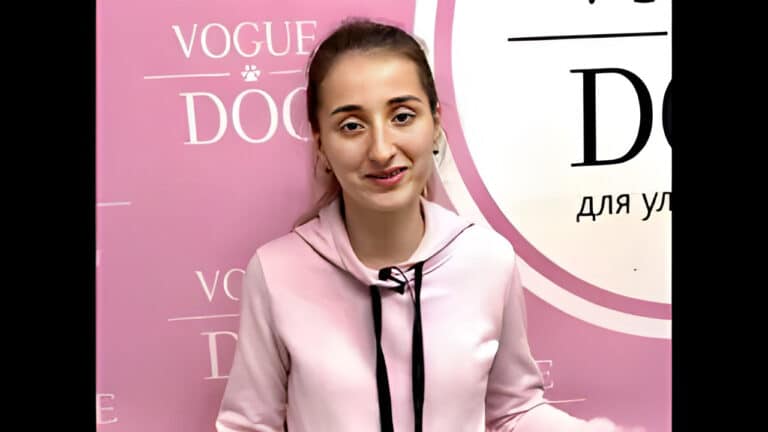 Дівчина в рожевому худі та світлими тінями на очах посміхається на фоні рожевого банера