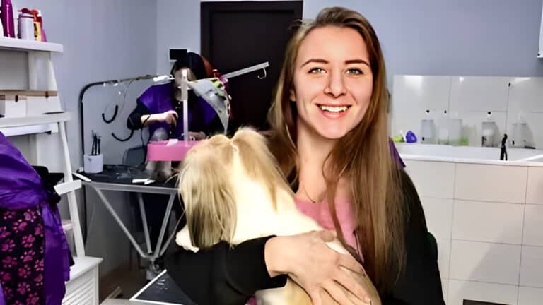 Позаду дівчини з ши-цу грумер працює над стрижкою собаки