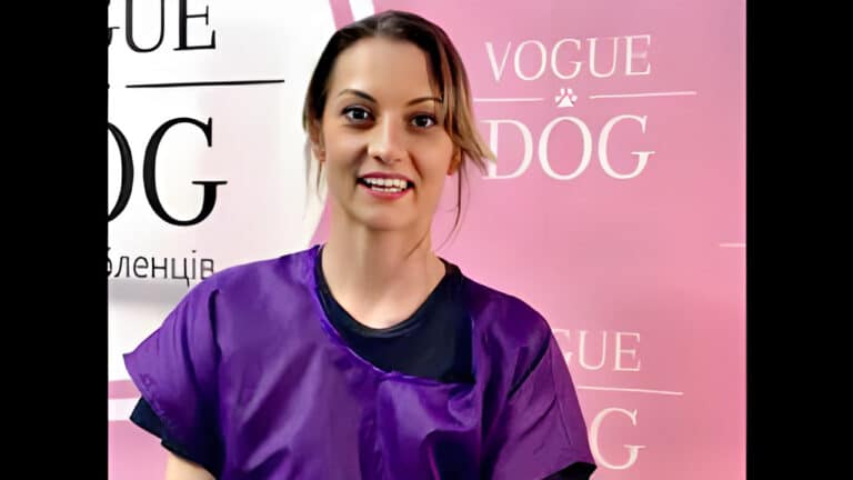 Дівчина в чорній футболці та фіолетовій накидці відкрила рота на фоні рожевого банера, промовляючи слова