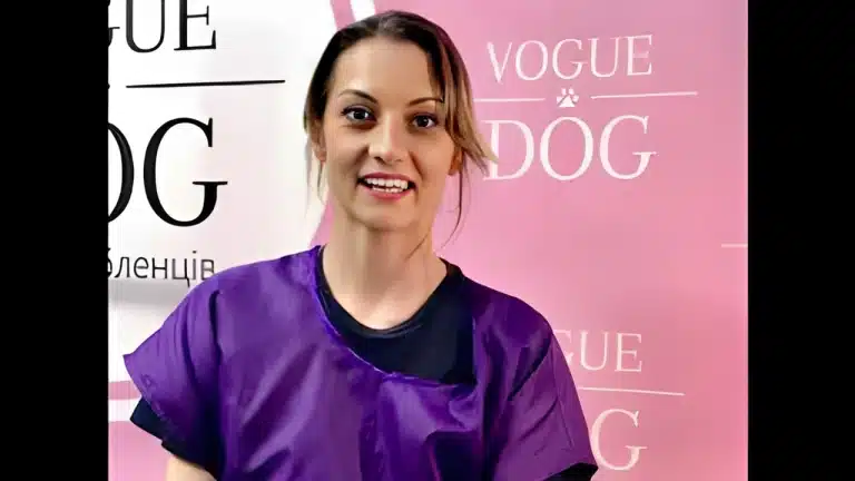 Дівчина в чорній футболці та фіолетовій накидці відкрила рота на фоні рожевого банера, промовляючи слова