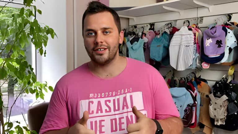 Хлопець в рожевій футболці показує два великих пальці біля стенда з одягом для собак