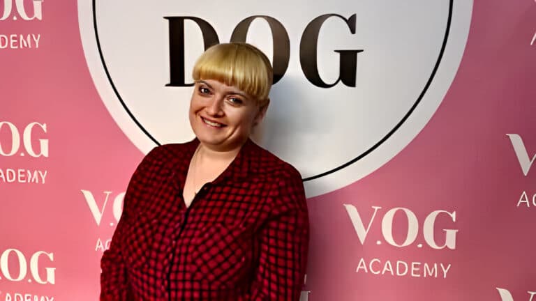 Жінка зі світлим волоссям та чубчиком на голові вдягнута в чорно-червону сорочку, яка не зливається з кольором стіни