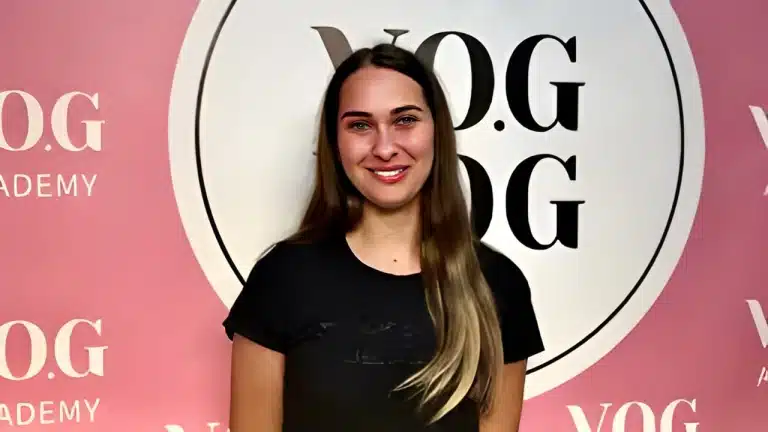 Дівчина в чорній футболці, яка стоїть перед рожевим банером, має світлі кінчики на коричневому волоссі