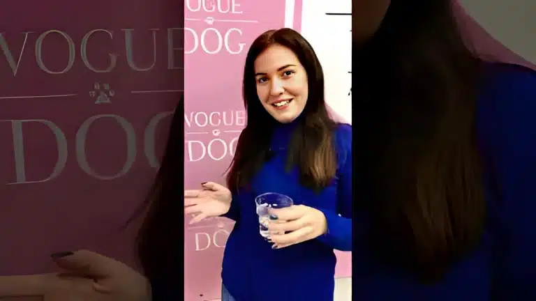 Дівчина в синьому гольфі та з синім манікюром тримає в руці прозору склянку з водою