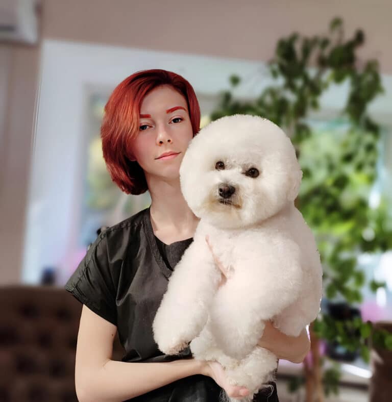 Дівчина з червоним волоссям та такими ж бровами тримає в руках білого бішона з круглою головою