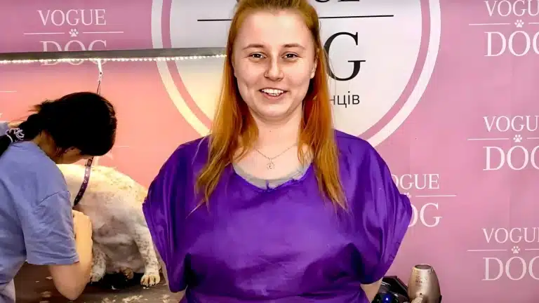 Рудоволоса дівчина з сережкою у носі склала руки за спиною та посміхається на камеру