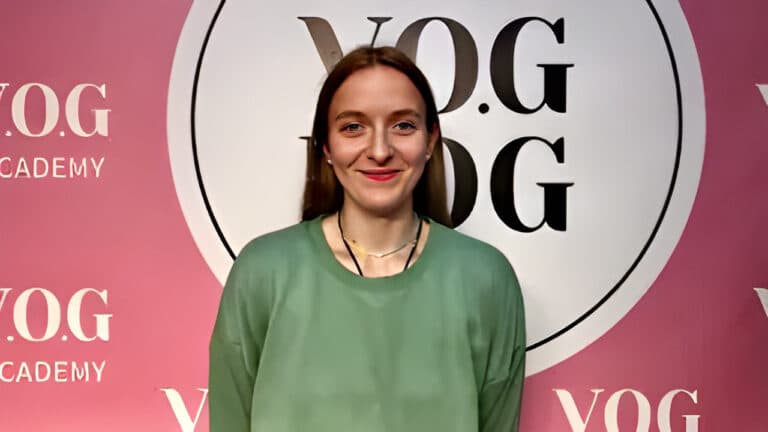 Дівчина в зеленому худі рівненько стоїть біля рожевого банера Академії