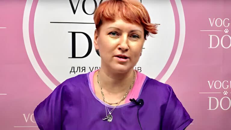 Дівчина з короткою стрижкою має на шиї декілька ланцюжків, які звисають поверх фіолетового одягу