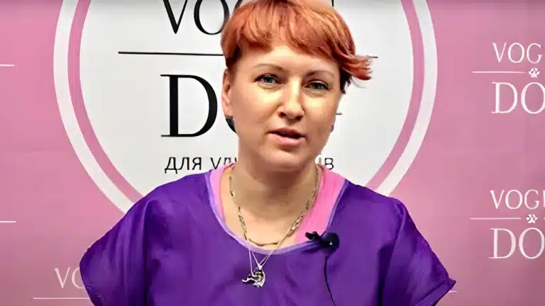 Дівчина з короткою стрижкою має на шиї декілька ланцюжків, які звисають поверх фіолетового одягу