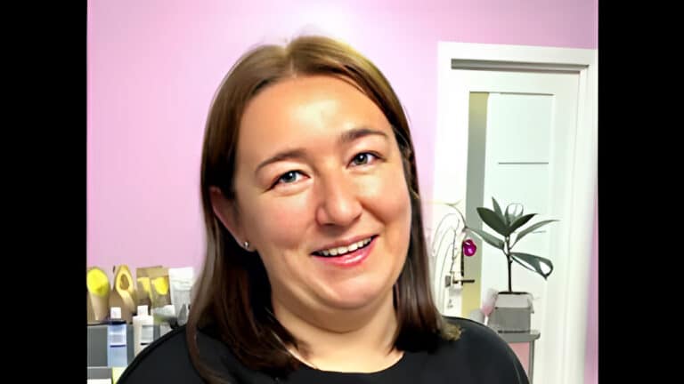 Жінка з маленькими сережками у вухах стоїть в кімнаті з рожевими стінами та білими дверима