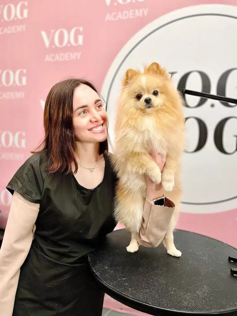 Дівчина тримає шпіца ззаду за грудку та посміхається йому