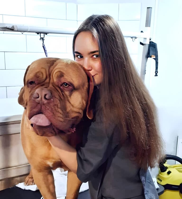 В кімнаті з білою плиткою дівчина обіймає гладкошерстого пса з величезною головою