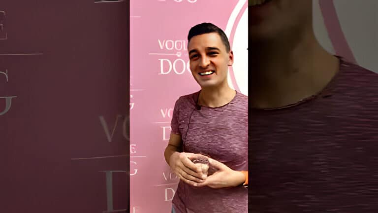 Чоловік в рожевій футболці щось тримає в руках біля банера з написами