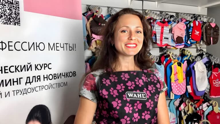 Дівчина з рожевою помадою тримає чорну сумку з рожевими відбитками лап на фоні стенда з одягом