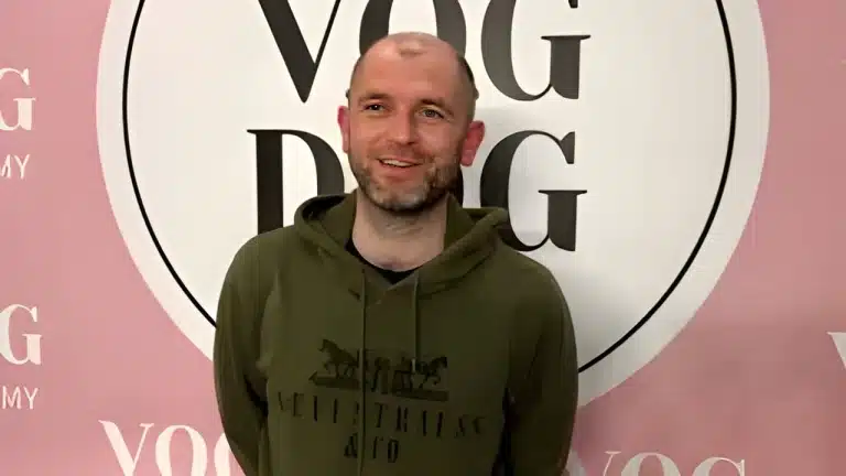 Чоловік в темно-зеленому худі склав за спиною руки та дивиться в бік