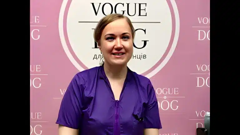 Жінка у фіолетовому одязі стоїть на фоні рожевого банера з логотипом