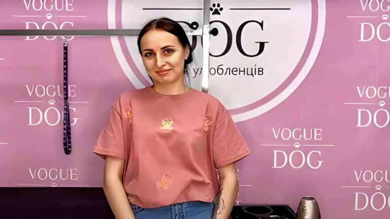 Чорнява дівчина в рожевій футболці сперлась на грумерський стіл з фіолетовою ринговкою