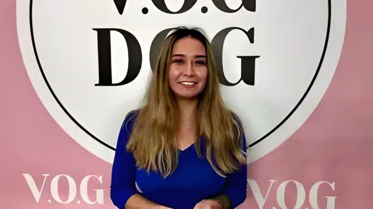 Дівчина в синьому гольфі має довге волосся, прямі брови та відкриту посмішку