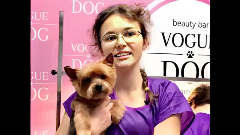 Дівчина з пухнастим волоссям та прямокутними окулярами тримає рукою йорка з забритими вушками