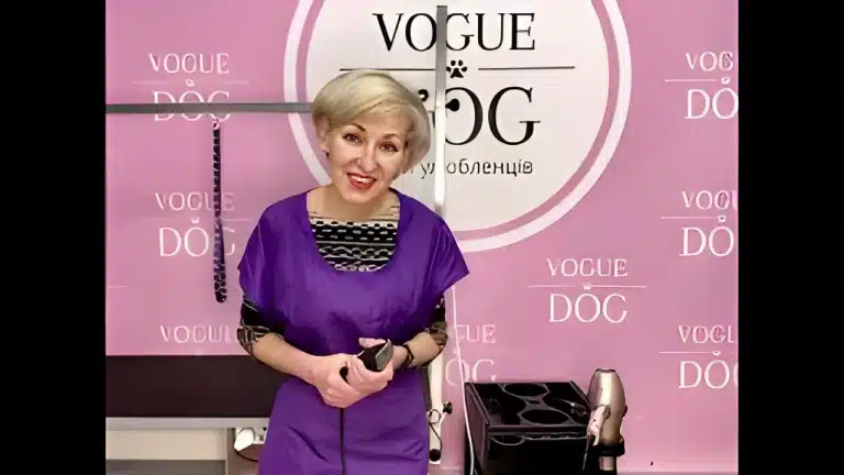 Жінка з білим волоссям вдягнута у фіолетову накидку, тримаючи в руках чорну машинку для стрижки