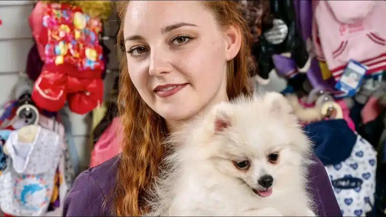 Рудоволоса дівчина у фіолетовій формі тримає в руках шпіца з круглими вушками біля стіни з одягом