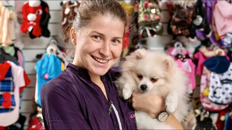 Синьоока дівчина у фіолетовій формі тримає однією рукою маленького шпіца на фоні великого асортименту одягу