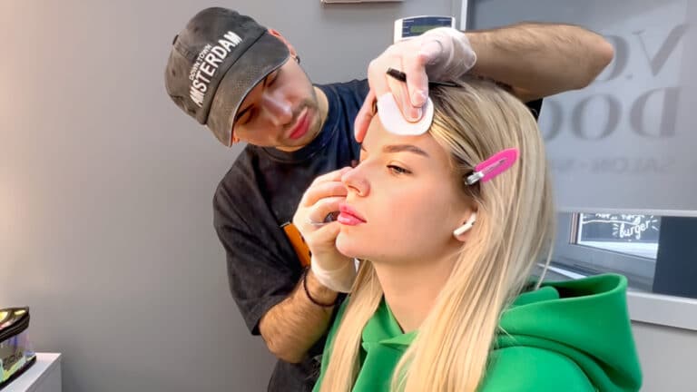 Хлопець в кепці проводить щіточкою по віях дівчини з білим волоссям