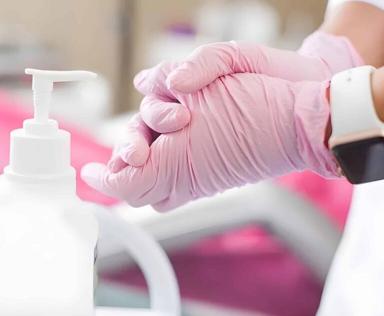 Людина в рожевих рукавичках склала руки разом біля дезінфектора з дозатором