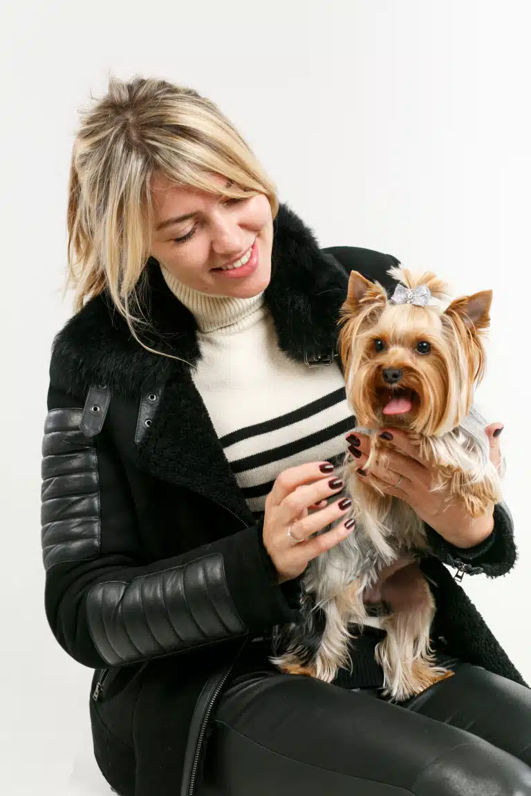 Дівчина в дублянці оглядає йорка з бантиком після стрижки