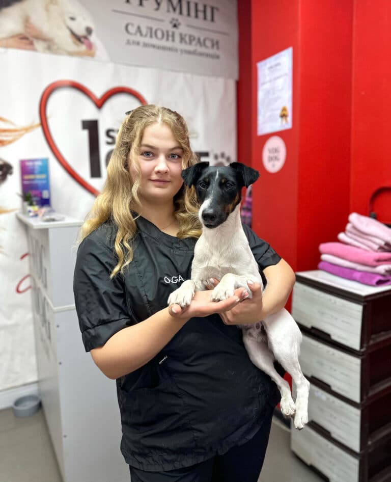 Дівчина з підкрученим світлим волоссям тримає на руках білого пса з чорною головою