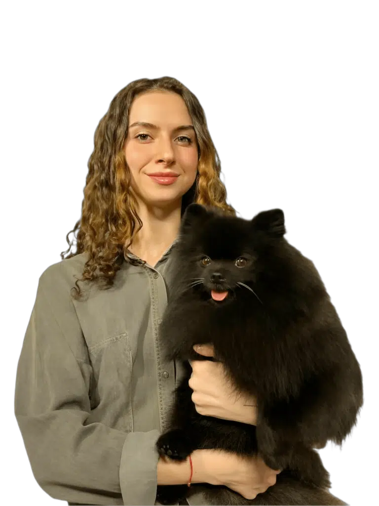 Дівчина з кучерявим волоссям та в джинсовій сорочці тримає в руках чорного шпіца з гострими вушками