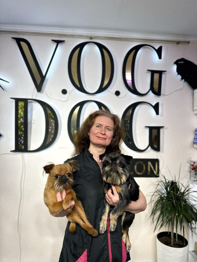 На фоні великих літер чорно-золотого кольору стоїть жінка з двома грифонами на руках