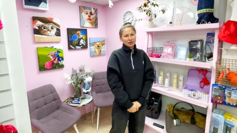 Дівчина в чорній спортивній кофті з білою блискавкою стоїть біля стенда з грумерським товаром