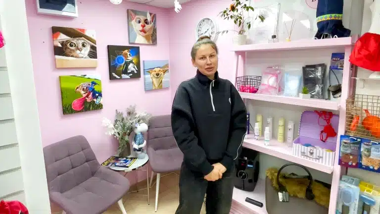 Дівчина в чорній спортивній кофті з білою блискавкою стоїть біля стенда з грумерським товаром