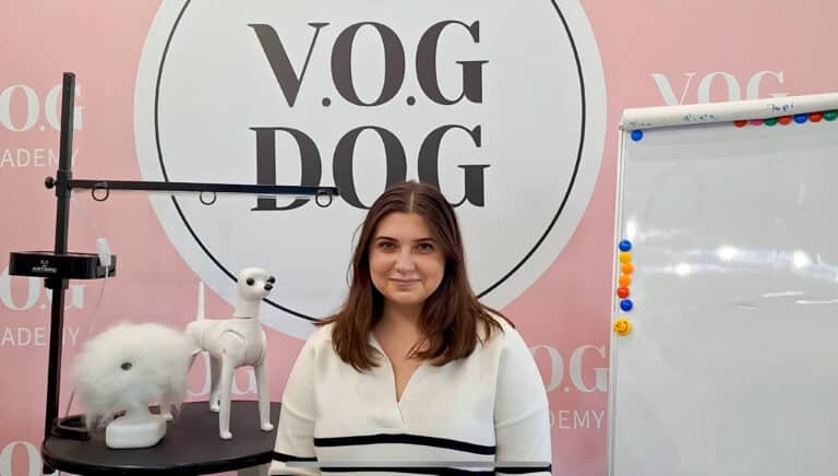 Дівчина в кофтині в смужку всміхається фотографу, сидячи на фоні банера з емблемою салону