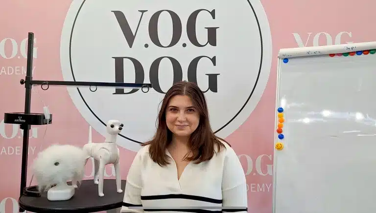 Дівчина в кофтині в смужку всміхається фотографу, сидячи на фоні банера з емблемою салону