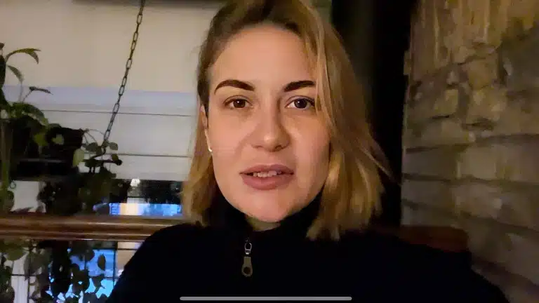 Дівчина зі світлим волоссям, але чорними бровами сидить у погано освітленому приміщенні