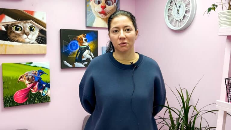 Дівчина в темно-синьому худі стоїть перед картинами тварин з мікрофоном на одязі