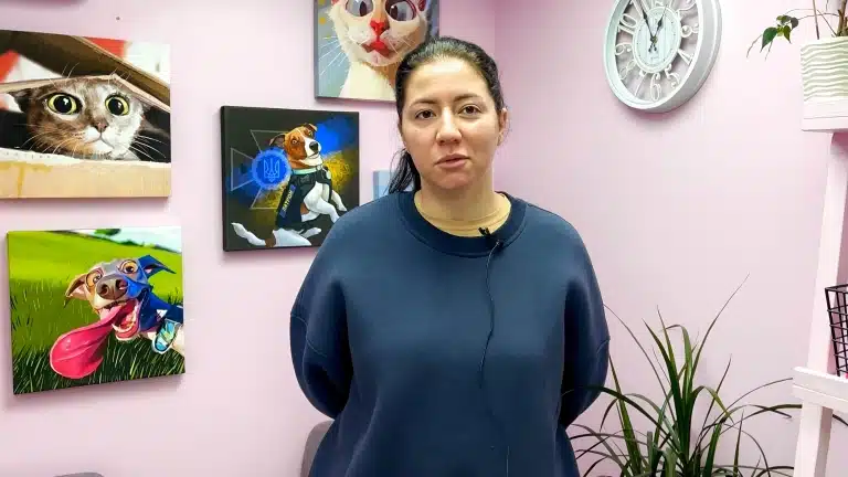 Дівчина в темно-синьому худі стоїть перед картинами тварин з мікрофоном на одязі