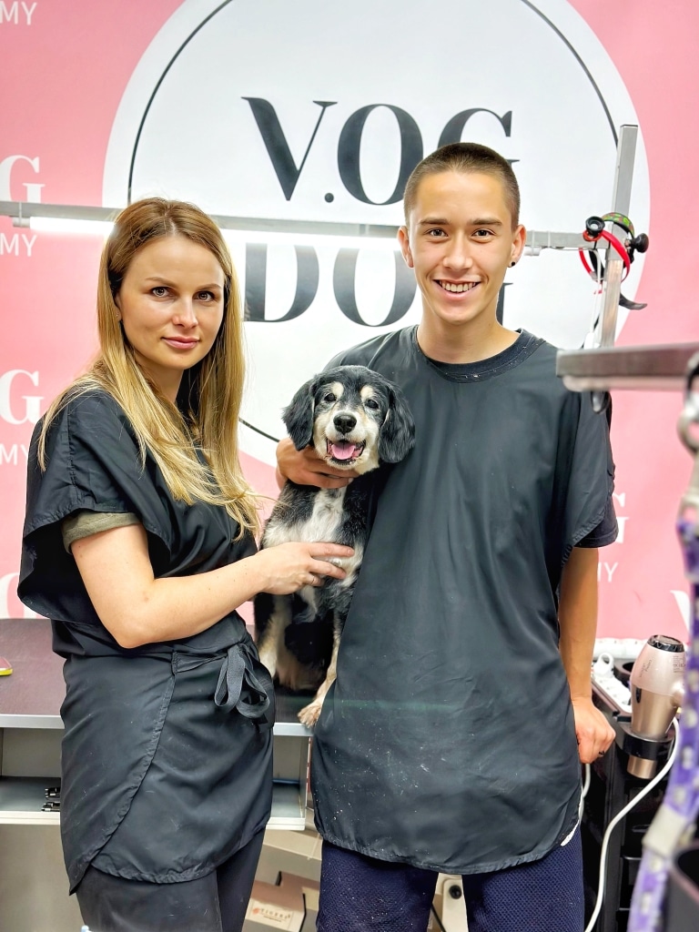 Хлопець з сережкою у лівому вусі обіймає песика правою рукою поруч з дівчиною