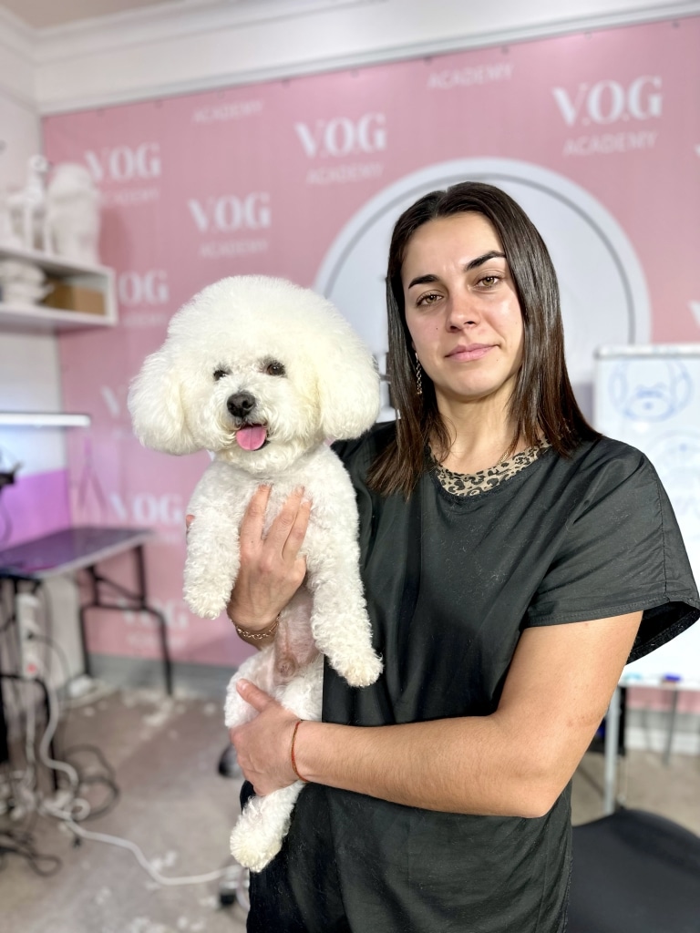 Дівчина з підстриженим бішоном стоїть посеред грумерської, повної шерсті на підлозі