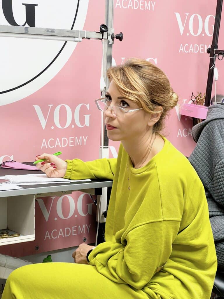 Жінка в салатовому костюмі сидить за грумерським столом та занотовує в зошиті зеленою ручкою почуте