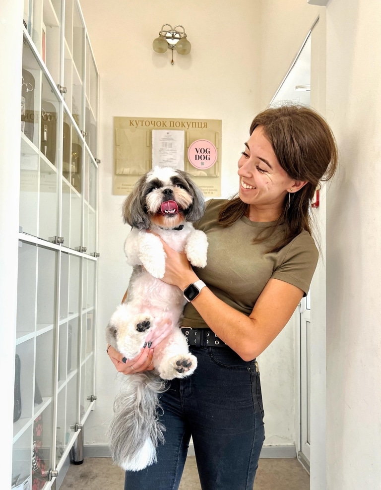 Дівчина в футболці хакі всміхається ши-цу після грумінгу в коридорі салону