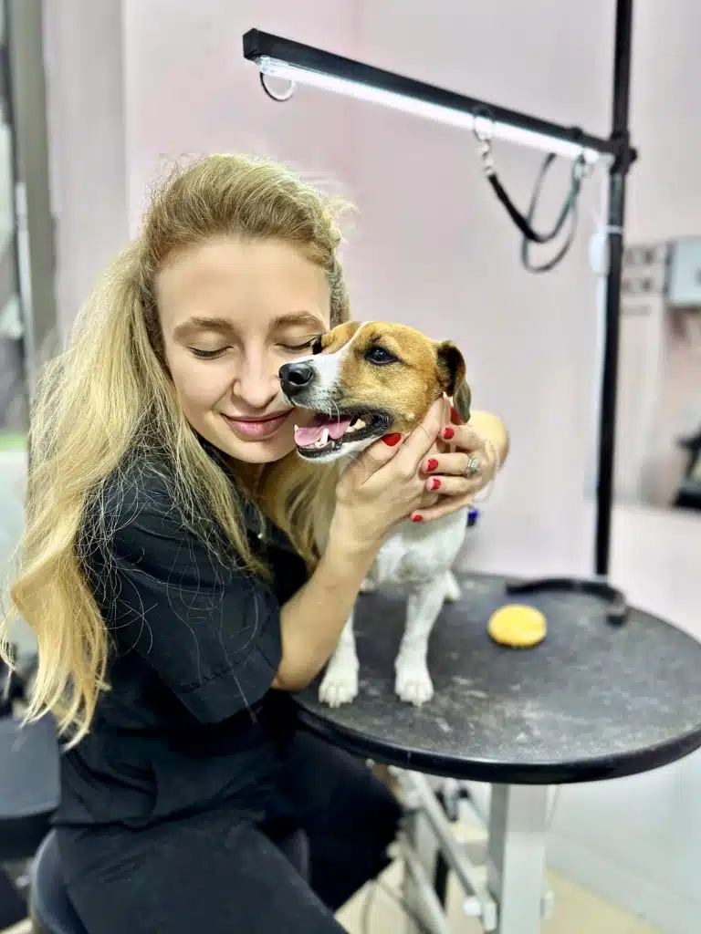 Грумерка з довгим волоссям обіймається в грумерській з джек-расселом